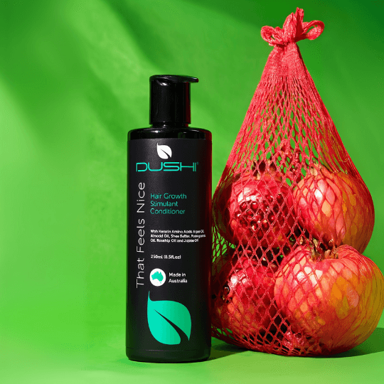 Dushi hair care product next to a bag of Pomegranates on a green background